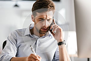 Serious business man talking by smartphone and writing something