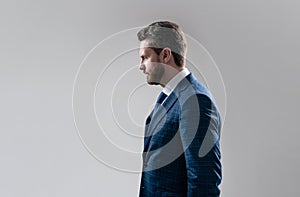 Serious business professional man stand sideway in suit grey background copy space, businessman