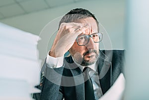 Serious business situation causing headache in office life, worried businessman looking at laptop