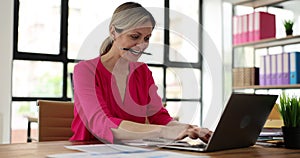 Serious business woman working at office desk with laptop clutches apencil in mouth