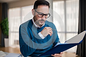 Serious businessman analyzing documents in file while sitting at the office desk