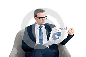 serious businessman in eyeglasses reading newspaper while sitting in armchair