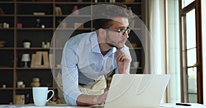 Serious businessman in glasses leaned at table working on laptop