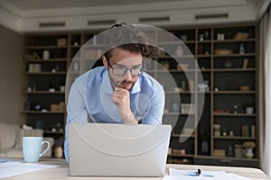 Serious businessman leaned at table staring at laptop screen