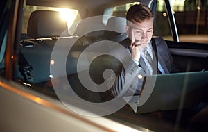 Serious businessman in moving car working on his laptop