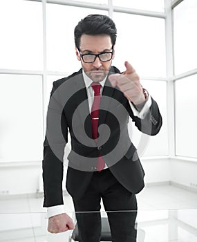 Serious businessman pointing his finger at you while standing in his office.