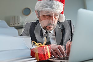 Serious businessman with Santa Claus hat typing on laptop computer keyboard during Christmas holiday