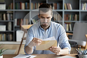 Serious businessman sit at desk holding envelope take out letter