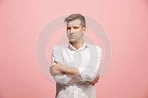 The serious businessman standing and looking at camera against pink background.