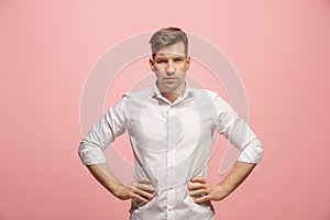 The serious businessman standing and looking at camera against pink background.