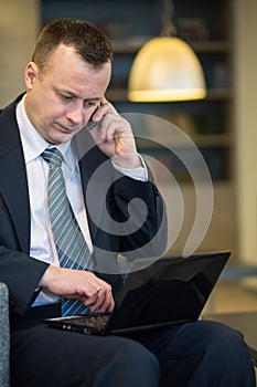 Serious businessman in suit and tie sitting with a laptop
