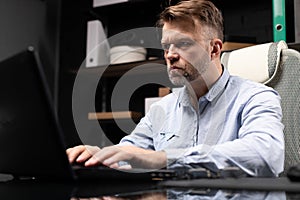 Serious businessman typing on laptop in stylish, modern office