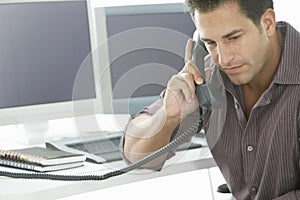 Serious Businessman Using Landline Phone At Desk