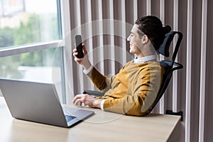 Serious businessman using smart phone and laptop at his office. Successful man employer sitting with cellphone in office interior