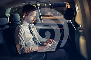 Serious businessman working late in car on laptop