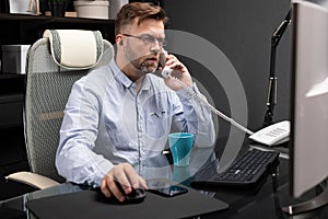 Serious Businessman working in office at computer Desk and talking on landline