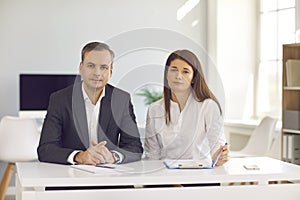 Serious businesspeople sitting at office desk and looking at camera during work meeting or interview