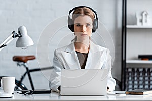 Serious businesswoman in headphones sitting at computer desk