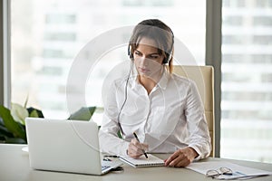 Serious businesswoman in headphones watching webinar on laptop m