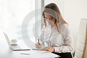 Serious businesswoman taking notes during routine office morning