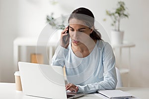 Serious businesswoman talking by phone working at laptop