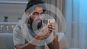 Serious busy Arabian Indian man bearded male in glasses typing browsing in smartphone texting chatting using mobile app