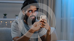 Serious busy Arabian Indian man bearded male in glasses typing browsing in smartphone texting chatting using mobile app