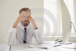 Serious busy businessman reads working documents sitting at a table with a computer in the office.