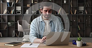 Serious busy man sit at workplace desk texting on laptop