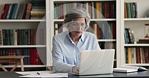 Serious busy mature business woman in glasses working at laptop
