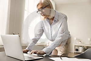 Serious busy older business leader woman typing on laptop