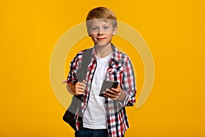 Serious calm cute caucasian young boy student with backpack typing on smartphone