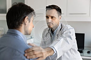 Serious caring doctor touching patients shoulder with sympathy photo