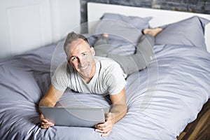 Serious casual young man using laptop in bed at home