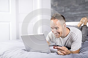 Serious casual young man using laptop in bed at home