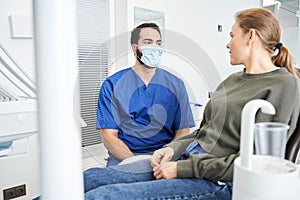 Serious caucasian lady in dentist chair asking her doctor for something