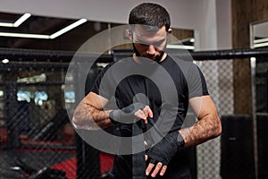 Serious Caucasian Male Kickboxer Fighter Preparing For Fight, Wrapping Hand In Bandage