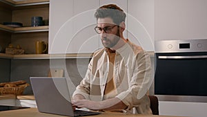 Serious Caucasian man browsing internet service chatting online in social media renter with laptop at kitchen food