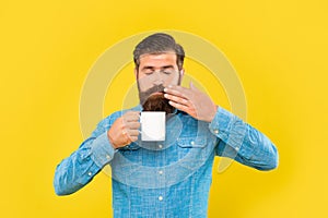Serious caucasian man with closed eyes smelling coffee holding hot cup yellow background