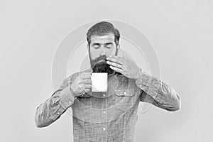 Serious caucasian man with closed eyes smelling coffee holding hot cup yellow background