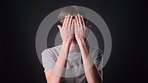 Serious Caucasian Man Covering Face with Hands on black Background