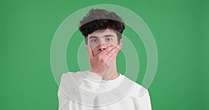 Serious caucasian man covers his mouth with his hand on a green background