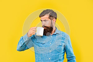 Serious caucasian man drinking coffee from mug yellow background