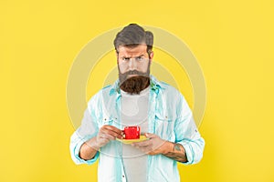 Serious caucasian man hold cup and saucer yellow background, coffee