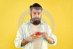 Serious caucasian man hold cup and saucer yellow background, tea