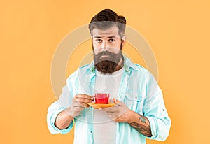 Serious caucasian man hold cup and saucer yellow background, tea