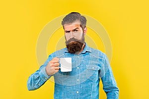 Serious caucasian man holding mug yellow background, tea break