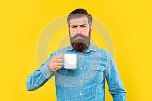 Serious caucasian man holding tea mug yellow background