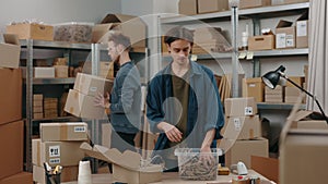 Serious caucasian man packing cupboard box with special filling while his male caucasian colleague sorting through