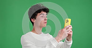 Serious caucasian man texting on the phone on a green background